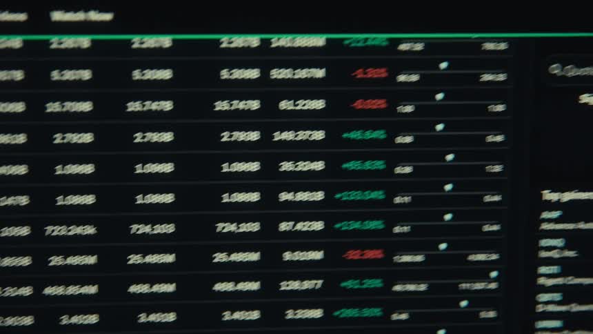 The screen of a computer monitor displays a scrolling list of cryptocurrency exchange rates and market data