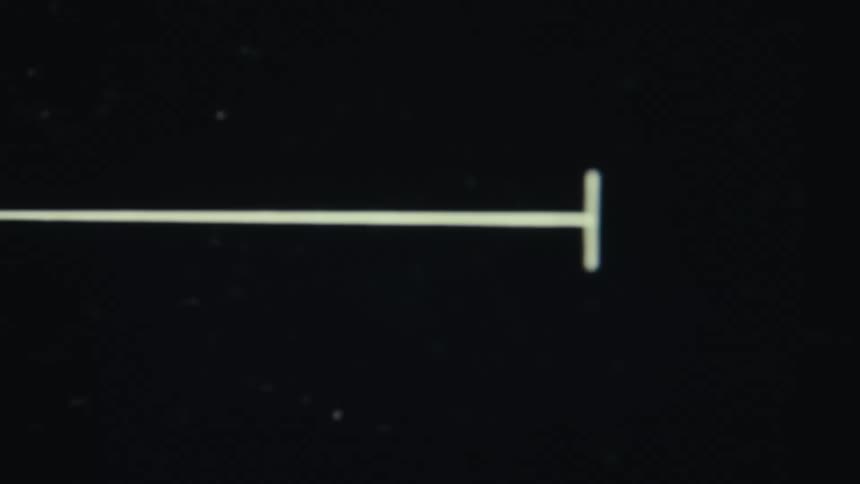 A closeup shot shows a white crosshair appearing on a black screen with a horizontal line pulsing back and forth the camera quickly moves to reveal a persons face as the crosshair stops and points at them