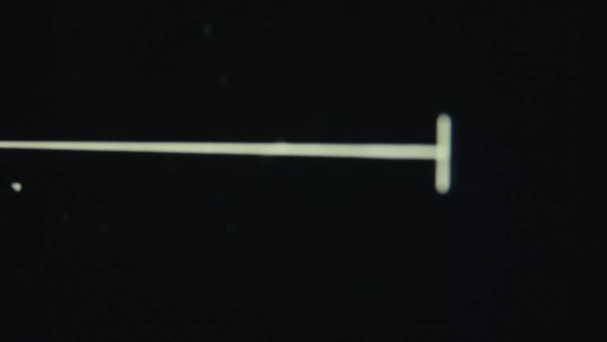 A thin white line with a small white vertical line at the end moves across a dark screen