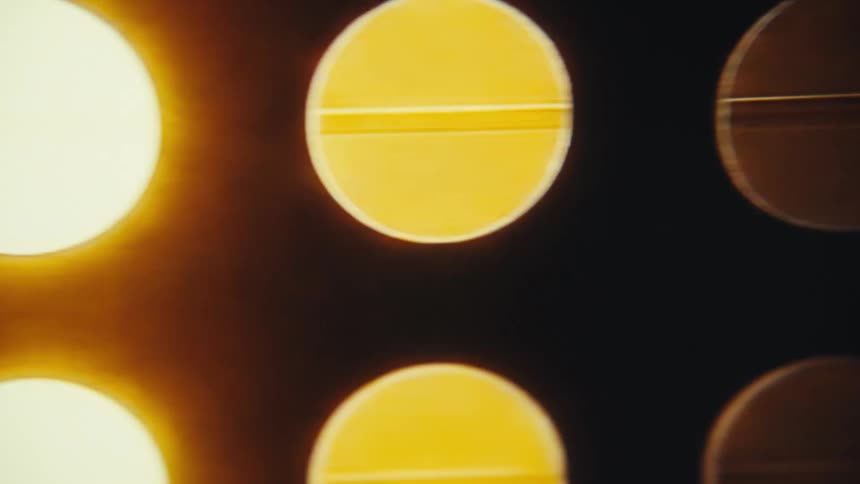 A closeup shot of circular stage lights shows them slowly dimming and brightening in a warm golden hue the camera pans across the light board as the lights change creating a dynamic background