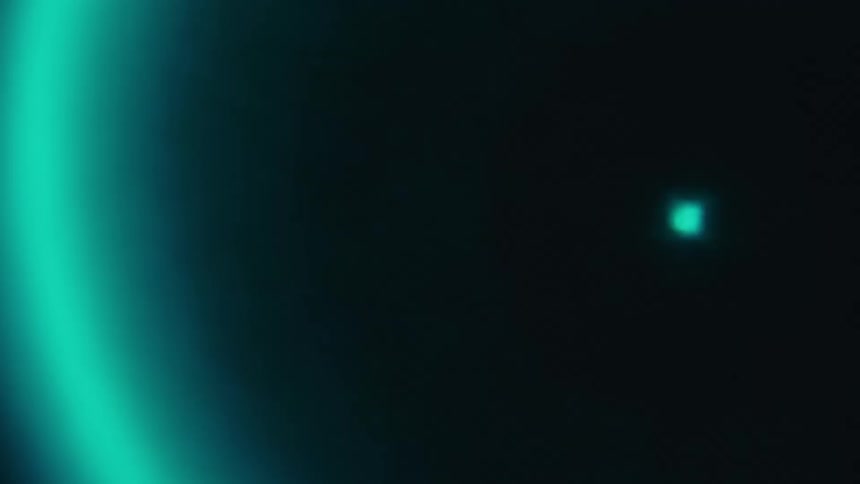 A bright teal light with a glowing halo and a slight lens flare is shown against a dark background pulsing in circles