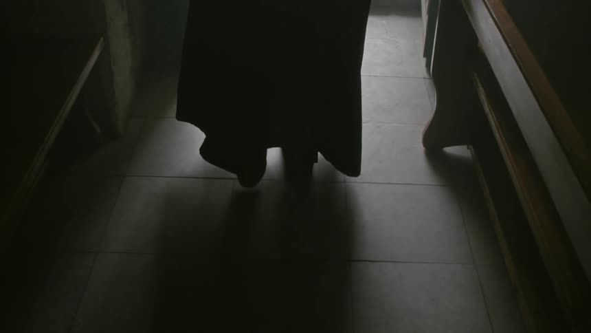A robed clergyman enters a dark room