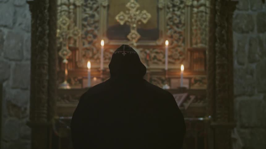 A man in black kneels before an alter