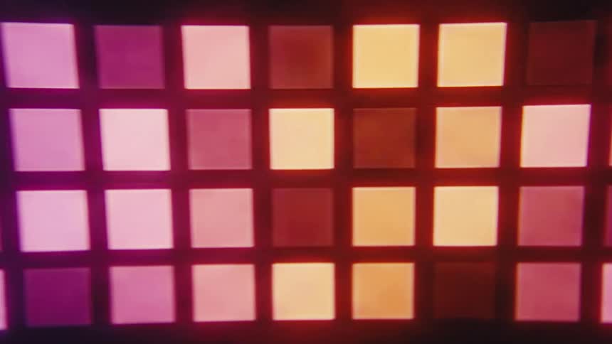 Disco light reflecting in a dark room casting different colors in a series of small glowing squares