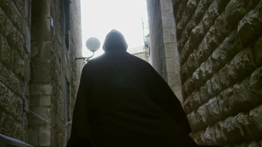 A man in robes walks down an alley