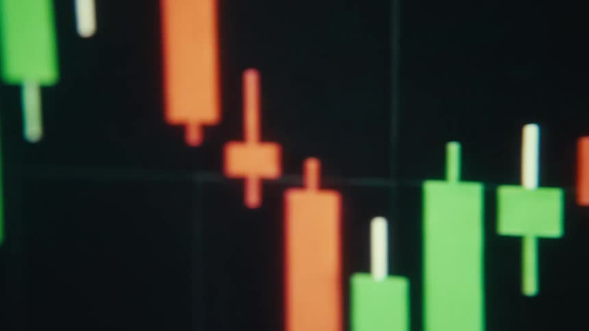 A monitor displays a stock market candlestick chart with green and red candles moving across a dark grid