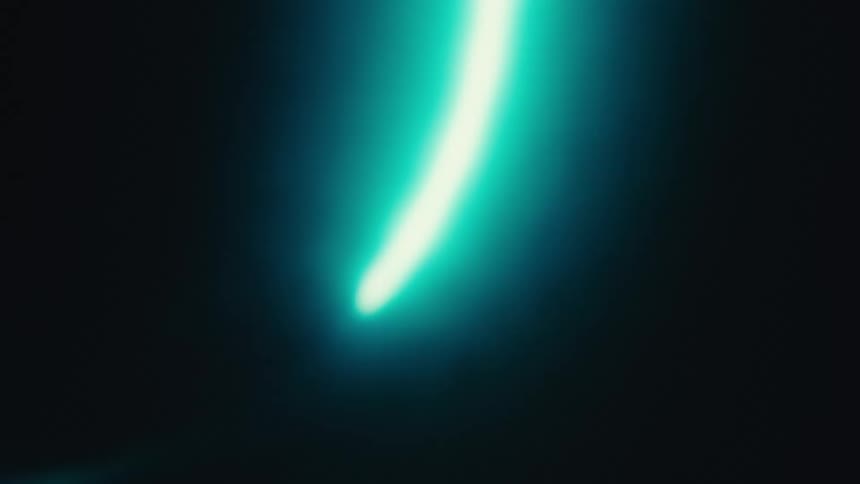 A vibrant bright turquoise light moves in a curved line on a black background with a hazy bloom effect