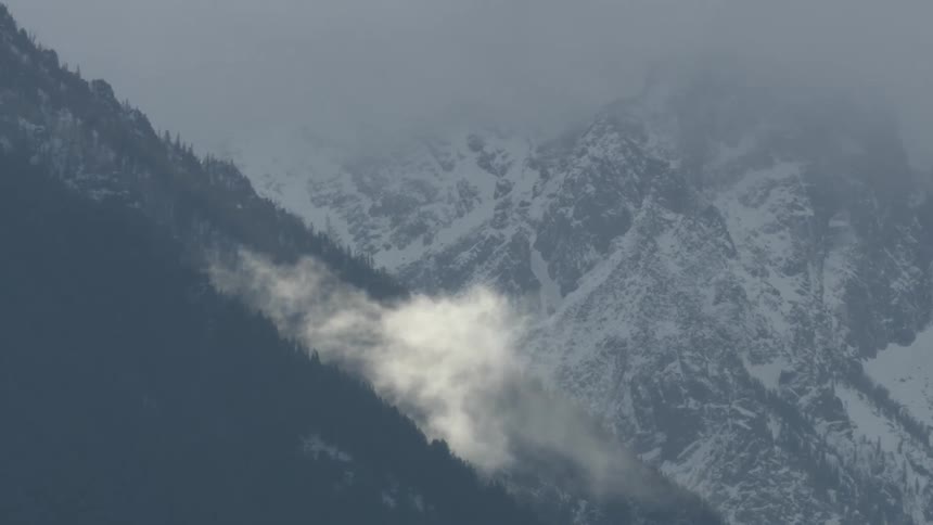 Low cloud hovers over dark hillside in front of snowy mountains