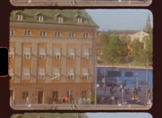 A film strip frame shows a vibrant city street with a yellow building in the foreground crowds of people walking in the background and a bell tower rising in the distance