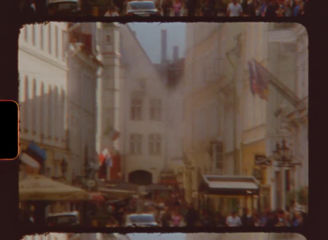 Busy street with pedestrians cars and flags between historic buildings