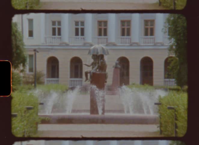 A statue in the middle of a fountain in front of a building with water sprinkling from the fountain