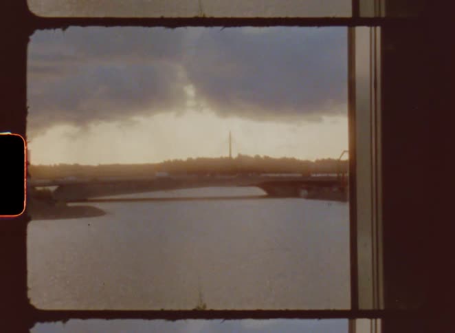 A cityscape and river are viewed through a film frame with visible sprockets as the camera pans down