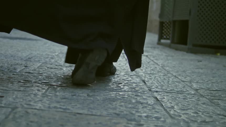A man in priest's vestments is walking on a stone path in a city