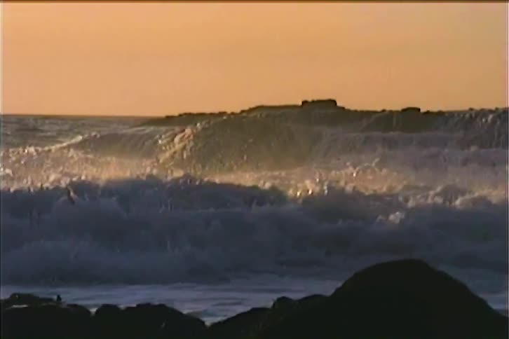 Wave crashing strongly against dark rocks at sunset