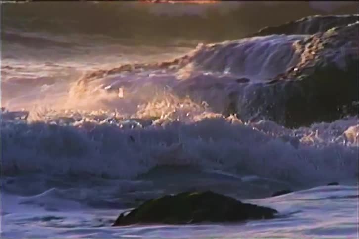 Waves crashing aggressively on a rocky shoreline during a sunny evening