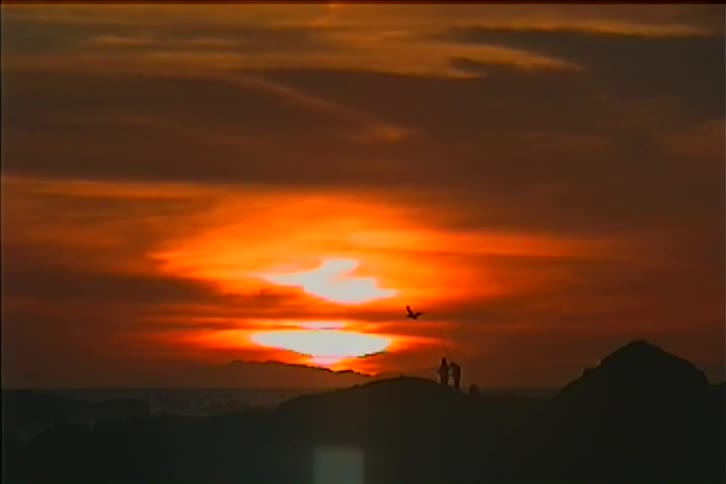 People stand close together on a hill silhouetted by the setting sun