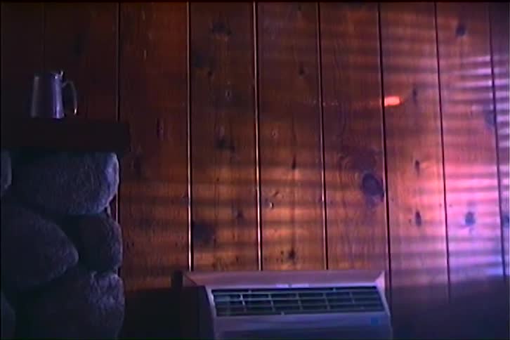 Sunlight filtering through blinds projected on a wooden wall with stone fireplace and metal pitcher