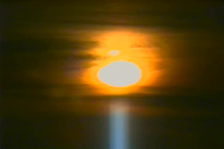 This grainy vintagestyle video shows a large glowing sun in the center of the frame the sky is dark and hazy with light streaks suggesting rain falling in front of the sun