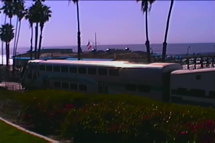 A train is traveling along a track by the beach at midday