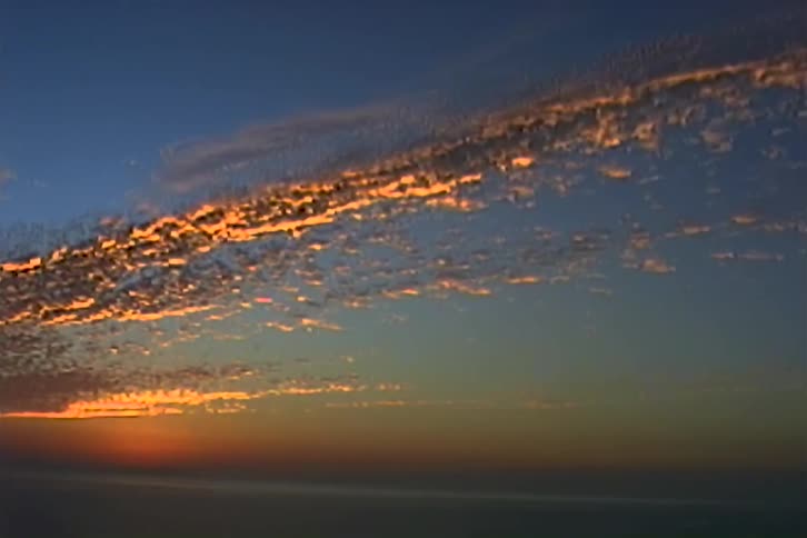 The first line shows a beautiful wide shot of an ocean sunset with the suns golden light reflecting on the water and a long streaky cloud formation glowing in the sky the second line shows the camera remaining static allowing the viewer to take in t