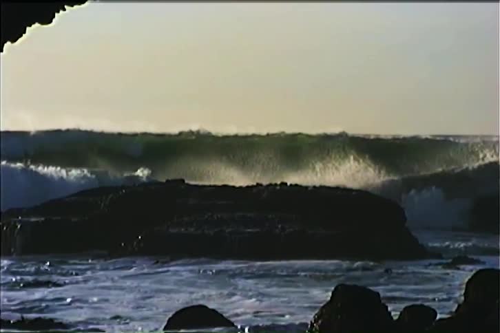 An ocean with heavy waves crashing onto rocks at the shore at midday