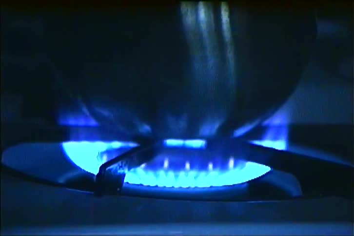 A teapot boils on a gas burner where intense blue flames ignite and heat the pot