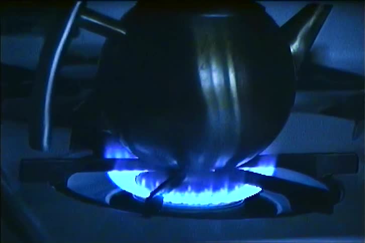 A kettle on a gas stove with blue flames in the kitchen