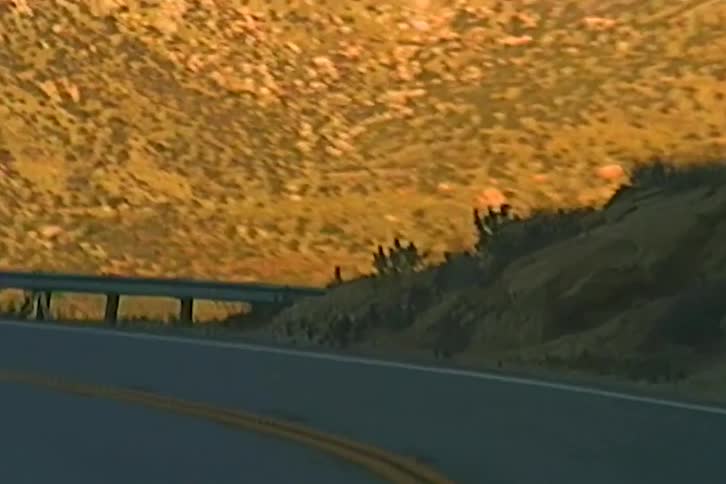 Highway guardrail overlooks a scrub filled valley in mountainous terrain