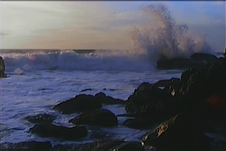 Waves crashing on dark rocks by the sea at sunset