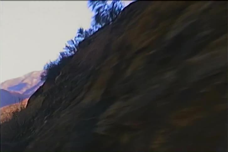 The camera rapidly pans across a massive rugged rock formation bathed in sunlight revealing its textured surface