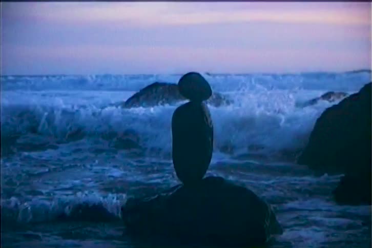 Ocean waves splashing against stacked rocks at the coast at sunset