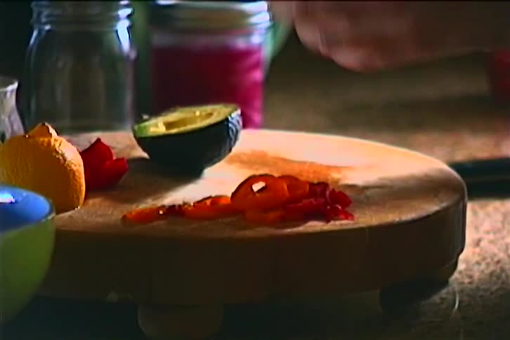 A womans hands taking out the seed from an avocado half then putting on a round cutting board next to tomato slices and the other half
