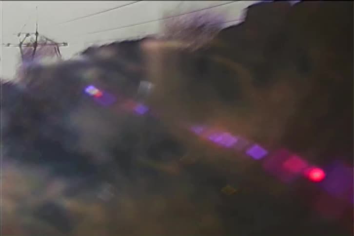This shaky vintagestyle video captures a scenic landscape at sunset the camera pans across a hillside with several power lines and towers while sun flares and visual distortion add a nostalgic dreamy effect
