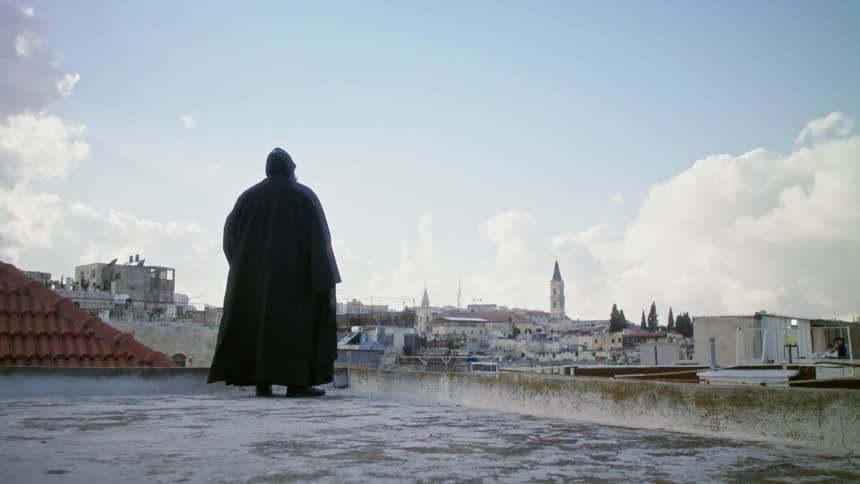 A robed clergyman stands on the roof of a building
