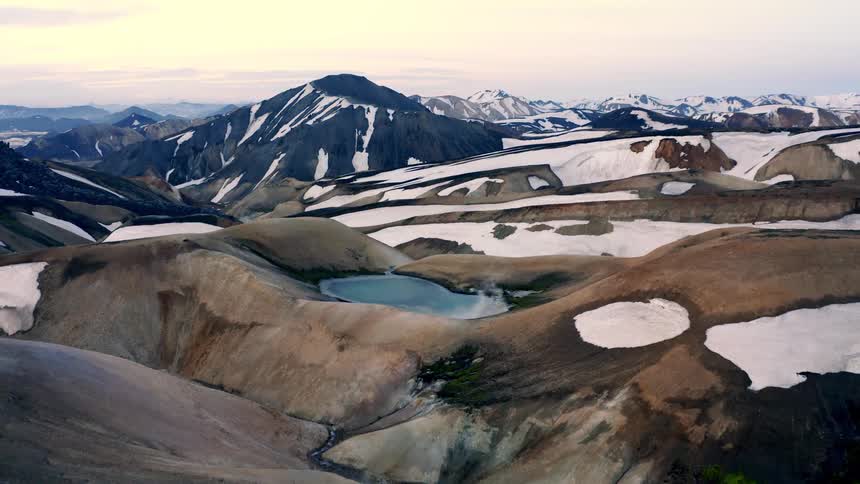 Mountain landscape with snow patches across rocky areas and a small lake in the center