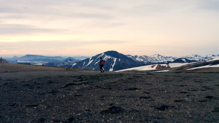 Photographer carrying a tripod walks across a plain near mountainous terrain on a cloudy winter day