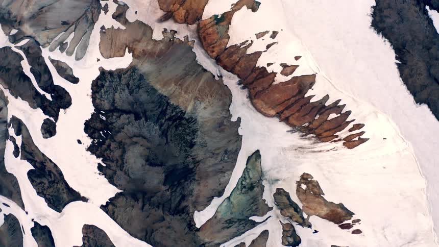 This satellite video shows an aerial view of a snowy mountainous landscape the video zooms out to reveal a wider view of the rocky peaks and valleys