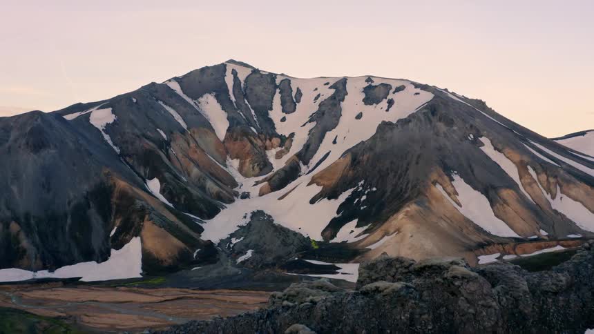 Rocky mountain with snow patches at sunset