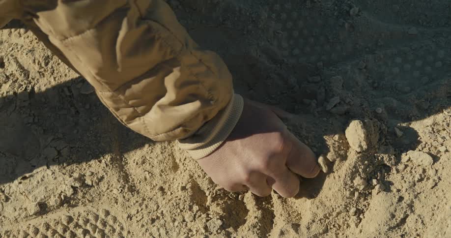 A person wearing a yellow jacket packing sand from the soil with bare hands on a sunny day