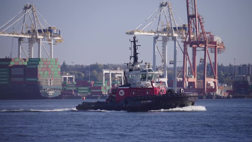 A boat sailing away from a distribution depot passing a large cargo boat loaded with shipping containers