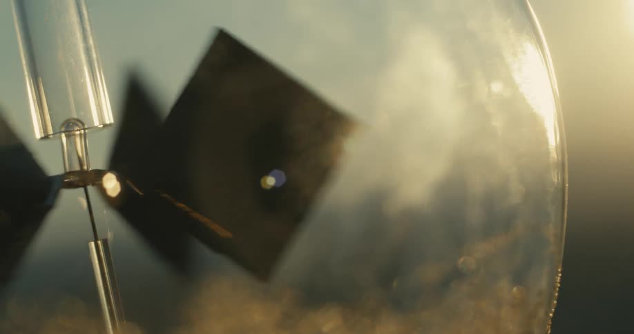 A radiometer with four vanes inside a glass bulb rotates illuminated by a light source and a blurry background