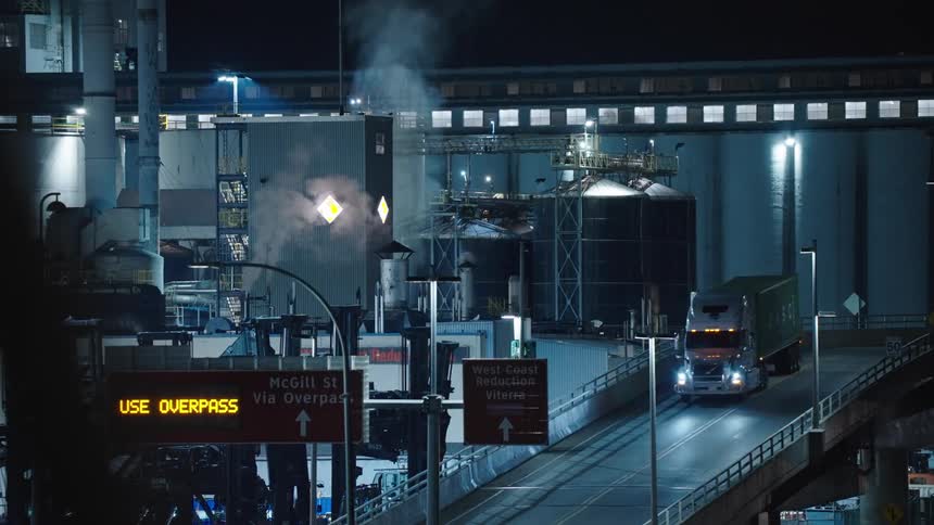 A commercial truck drives on a road leaving a large factory