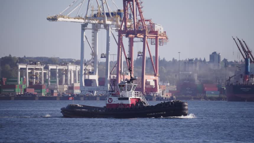A tugboat floats by a dockyard on a bright sunny day