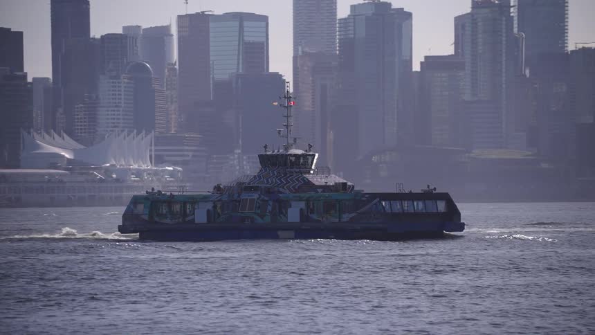 A ferry boat crossing a city river with the citys skyline behind it