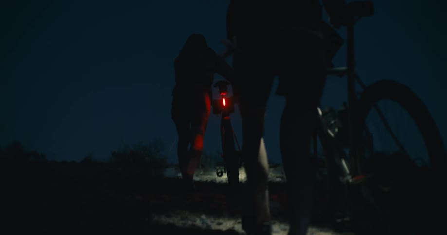 Cyclists pushing their bikes on a dark trail at night