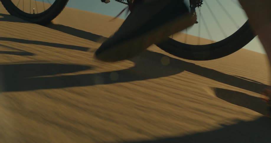 A person pushes a bicycle up a desert hill on a sunny day