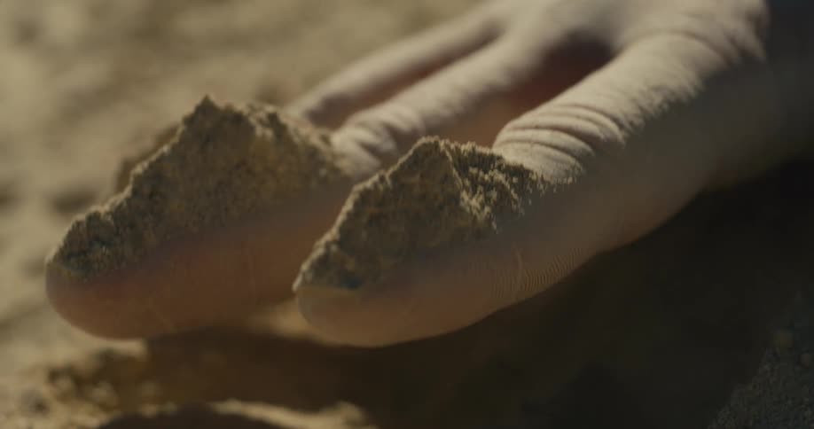 Hand pressing into the sand in closeup with highlighted texture