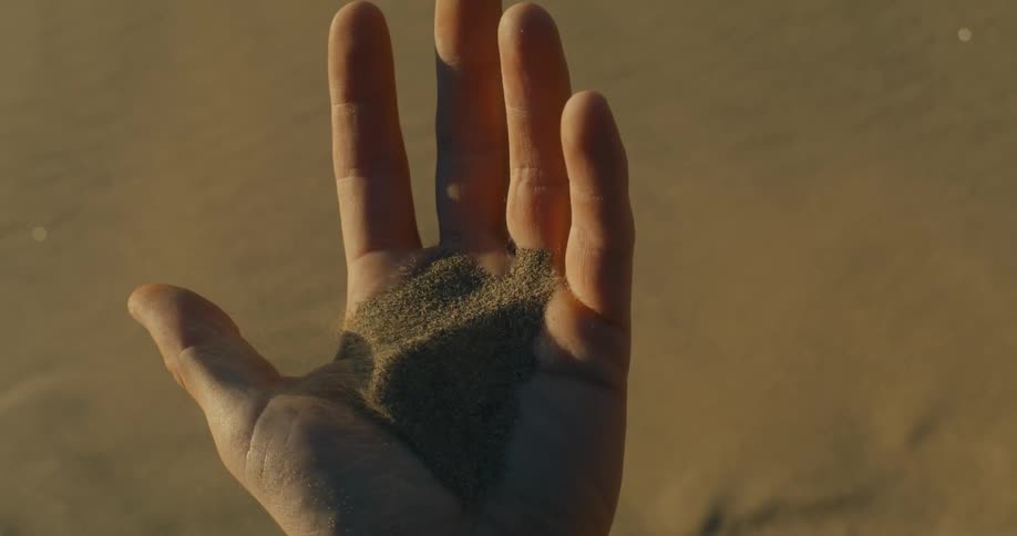 Open hand holding a handful of fine sand on the beach