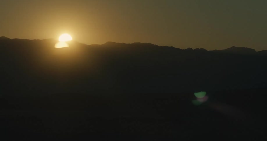 The sun rises behind the vast mountain range