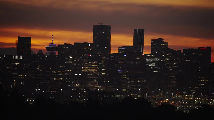 This shot captures the silhouette of a bustling city skyline at sunset the sky is a dramatic blend of orange pink and purple while the citys dark buildings are beginning to light up for the night